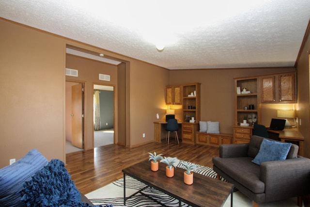 living area with built in study area, visible vents, a textured ceiling, and wood finished floors