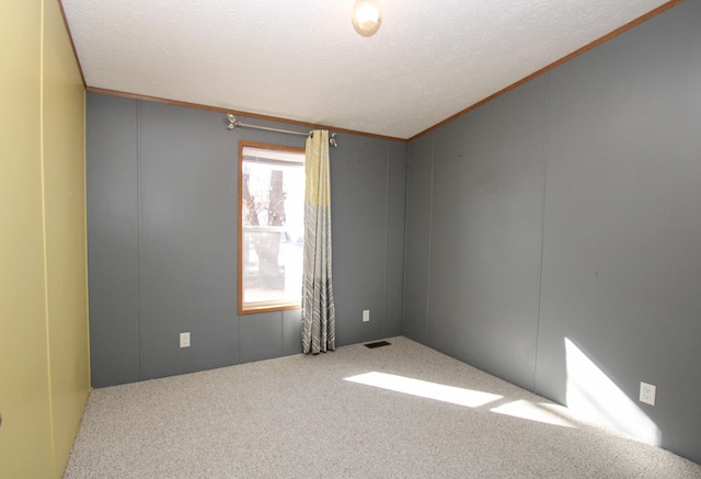 carpeted empty room with visible vents, crown molding, and a textured ceiling