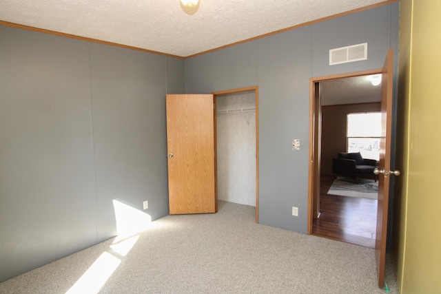 unfurnished bedroom featuring a textured ceiling, visible vents, a closet, carpet, and crown molding