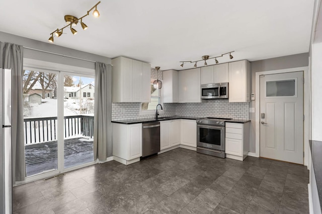 kitchen with appliances with stainless steel finishes, backsplash, dark countertops, and a sink