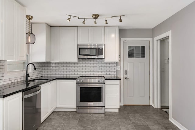 kitchen with tasteful backsplash, dark countertops, appliances with stainless steel finishes, white cabinetry, and a sink