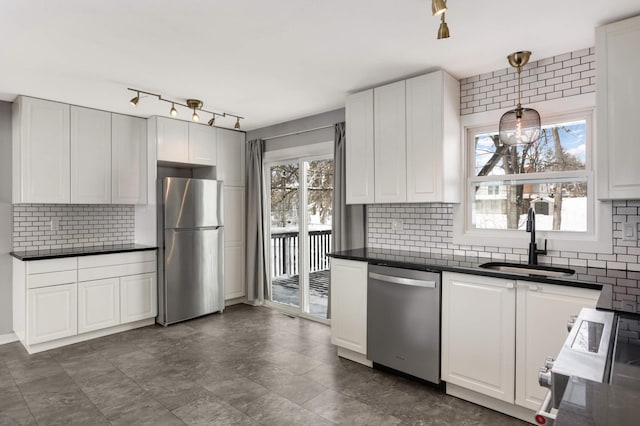 kitchen with appliances with stainless steel finishes, dark countertops, a sink, and white cabinetry