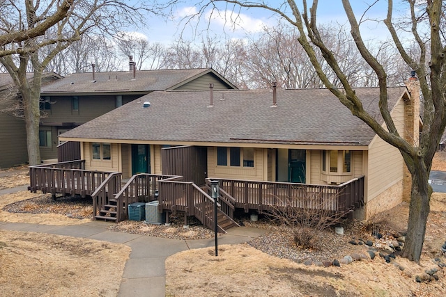 back of property with central AC unit, roof with shingles, and a chimney