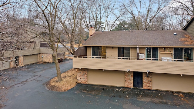 view of front of home with a garage, roof with shingles, a chimney, and aphalt driveway