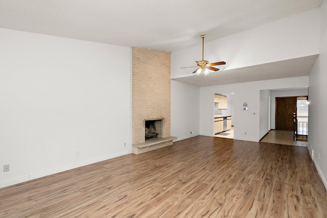 unfurnished living room with a ceiling fan, light wood-style floors, a fireplace, baseboards, and vaulted ceiling