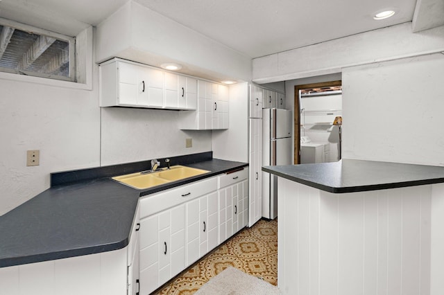 kitchen with freestanding refrigerator, a sink, white cabinets, dark countertops, and independent washer and dryer