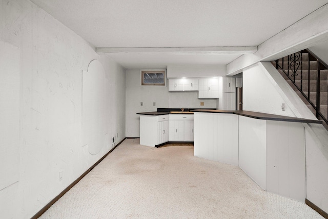 kitchen featuring dark countertops, light carpet, beam ceiling, a textured wall, and white cabinets