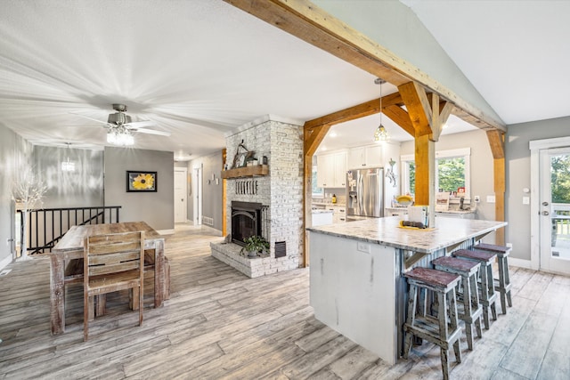 kitchen featuring light wood finished floors, light stone counters, a breakfast bar area, white cabinetry, and stainless steel refrigerator with ice dispenser