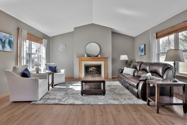 living area featuring a fireplace with flush hearth, baseboards, vaulted ceiling, and wood finished floors