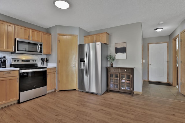 kitchen featuring tasteful backsplash, light countertops, light brown cabinetry, appliances with stainless steel finishes, and light wood-style floors