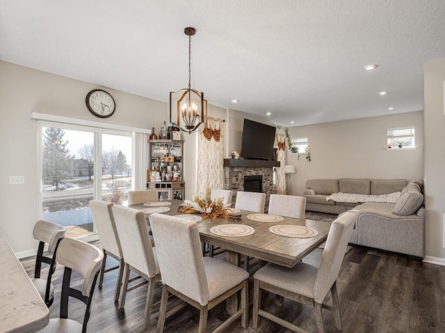 dining space featuring dark wood-style floors, baseboards, recessed lighting, a stone fireplace, and a textured ceiling