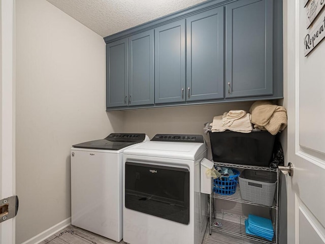 laundry room featuring a textured ceiling, cabinet space, light wood finished floors, baseboards, and washing machine and clothes dryer