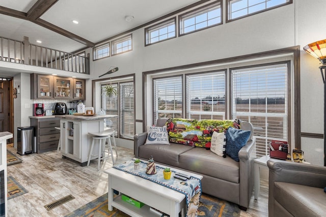 living room with visible vents, plenty of natural light, light wood-style floors, and beamed ceiling