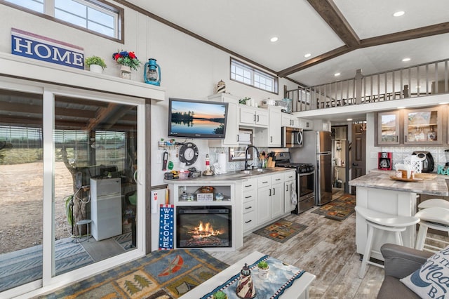 kitchen with light wood-type flooring, beam ceiling, white cabinets, stainless steel appliances, and a sink