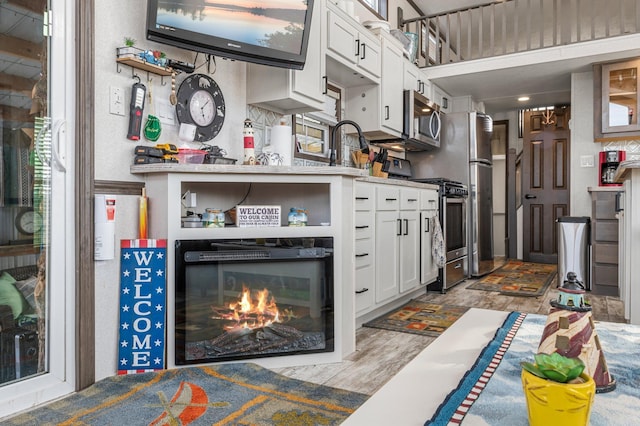 kitchen featuring a sink, open shelves, a glass covered fireplace, white cabinetry, and appliances with stainless steel finishes