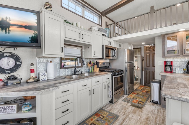 kitchen with light wood-type flooring, a sink, appliances with stainless steel finishes, white cabinets, and light countertops