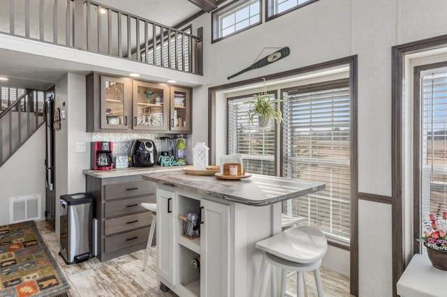 kitchen featuring visible vents, decorative backsplash, a kitchen breakfast bar, light wood-style floors, and glass insert cabinets