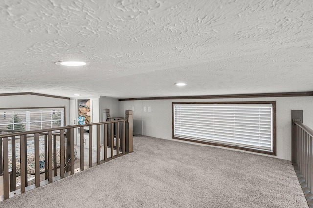 corridor featuring an upstairs landing, ornamental molding, a textured ceiling, carpet flooring, and a textured wall