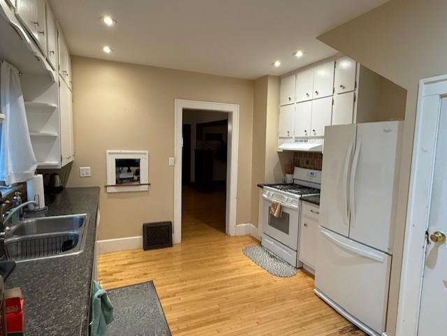 kitchen featuring dark countertops, visible vents, a sink, white appliances, and under cabinet range hood