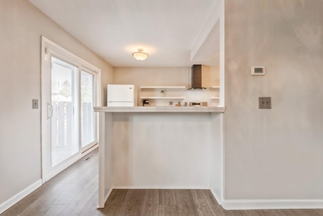 kitchen featuring wall chimney range hood, baseboards, wood finished floors, and freestanding refrigerator