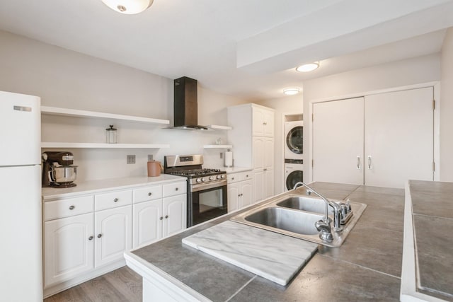 kitchen featuring a sink, freestanding refrigerator, stainless steel gas stove, wall chimney exhaust hood, and open shelves