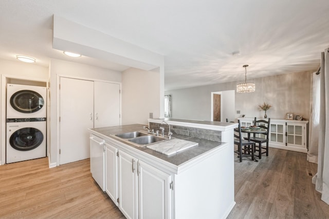 kitchen with light wood finished floors, stacked washing maching and dryer, a sink, white cabinets, and a chandelier