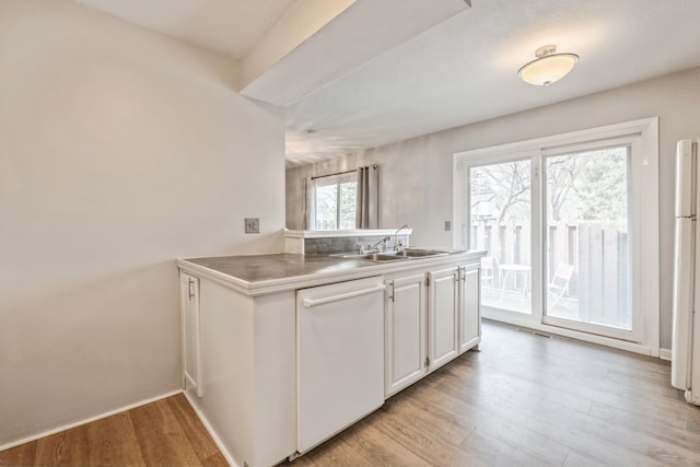 kitchen with white appliances, light wood-style flooring, a sink, light countertops, and white cabinetry