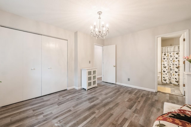 unfurnished bedroom featuring wood finished floors, baseboards, ensuite bath, a closet, and a chandelier