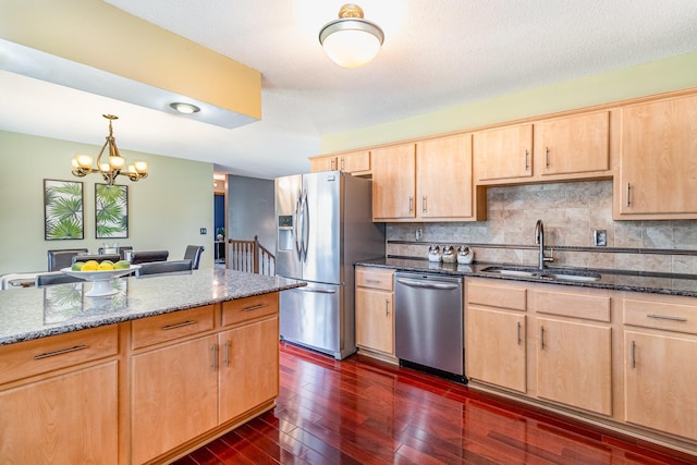 kitchen with light brown cabinets, a sink, dark stone countertops, dark wood-style floors, and appliances with stainless steel finishes