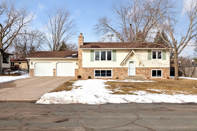 raised ranch with fence, driveway, a chimney, stone siding, and a garage