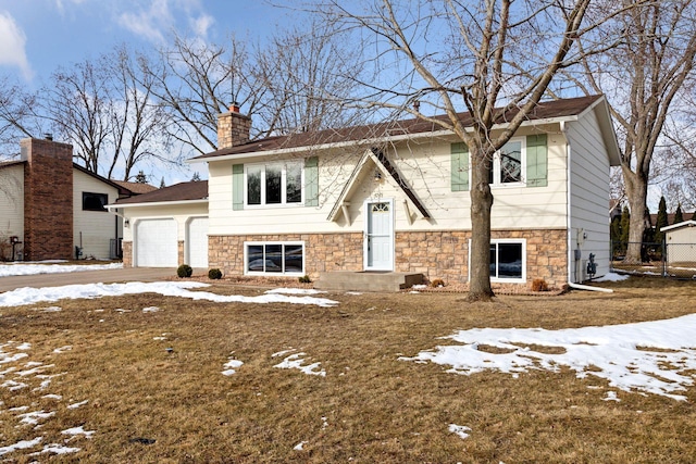 split foyer home with an attached garage, stone siding, driveway, and a chimney