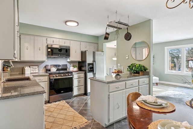 kitchen with a sink, stone countertops, backsplash, stainless steel appliances, and baseboards