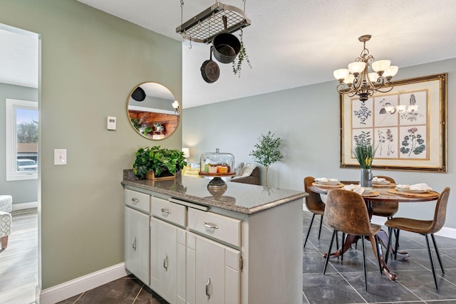 kitchen featuring baseboards, light stone counters, a peninsula, an inviting chandelier, and white cabinets