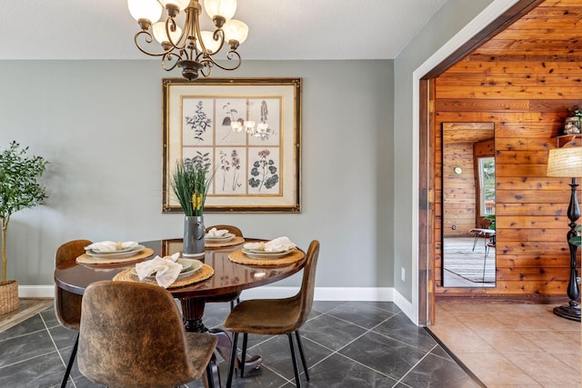 dining room featuring an inviting chandelier, wooden walls, dark tile patterned floors, and baseboards