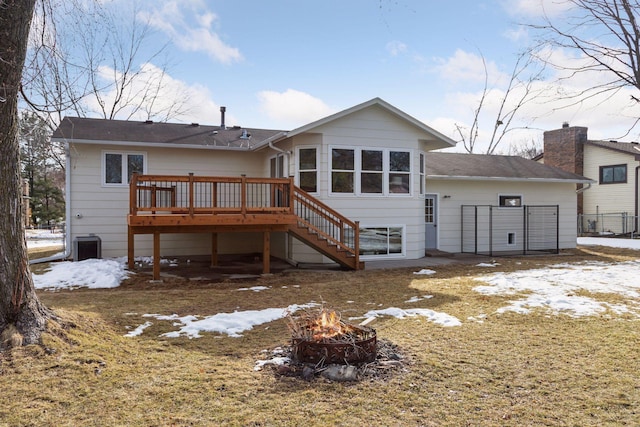 snow covered back of property featuring fence, a chimney, stairs, a fire pit, and a deck