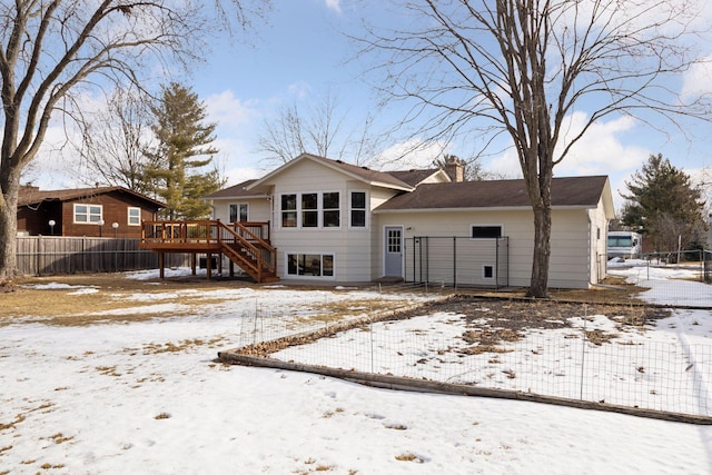 snow covered property with a wooden deck, stairway, a chimney, and fence