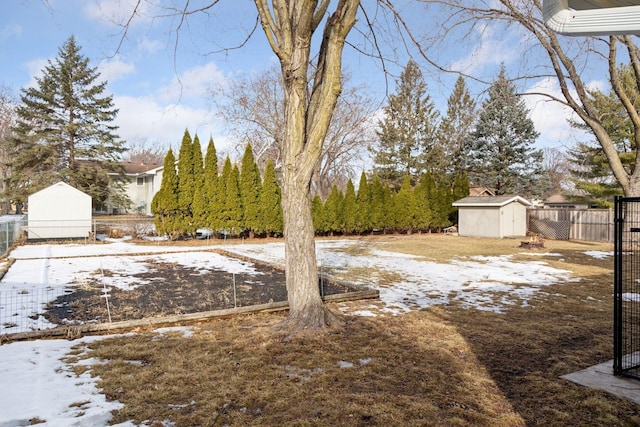 yard covered in snow featuring an outbuilding, a storage unit, and fence