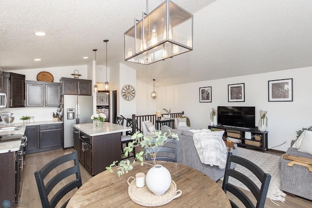 dining area with vaulted ceiling, a textured ceiling, a chandelier, and light wood-style flooring