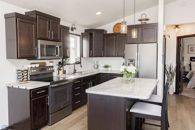 kitchen featuring appliances with stainless steel finishes, vaulted ceiling, dark brown cabinets, a kitchen bar, and a sink