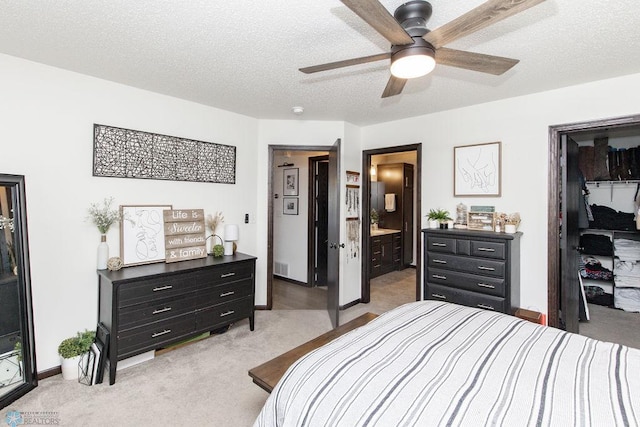 bedroom with a walk in closet, a closet, light carpet, connected bathroom, and a textured ceiling