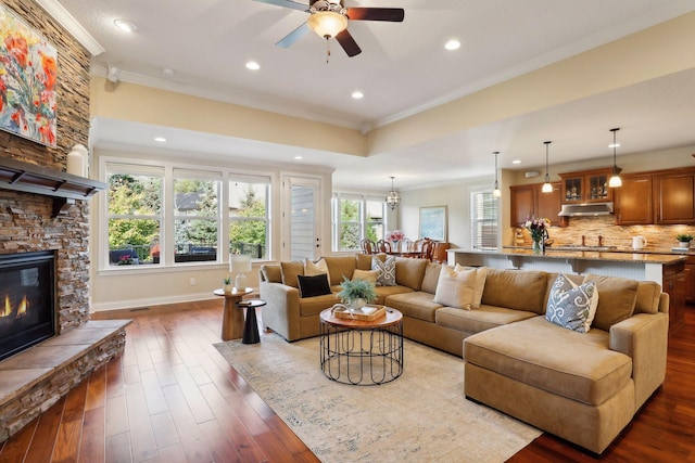 living room with a stone fireplace, recessed lighting, wood finished floors, and crown molding