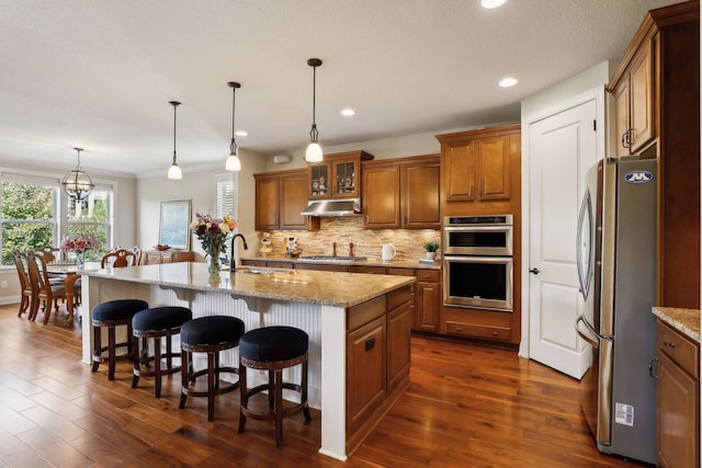 kitchen featuring a sink, stainless steel appliances, brown cabinets, and under cabinet range hood