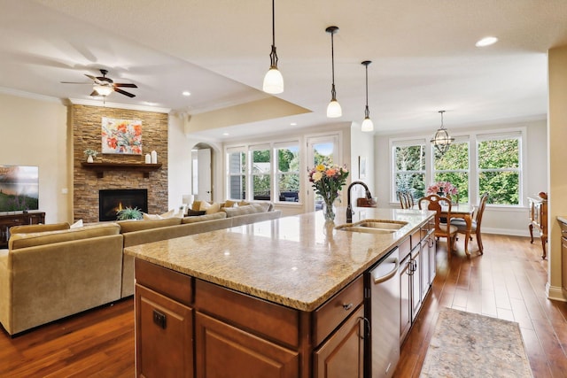 kitchen with a stone fireplace, light stone counters, dark wood-style flooring, a sink, and ornamental molding