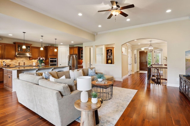 living area featuring baseboards, arched walkways, dark wood-style flooring, and ornamental molding