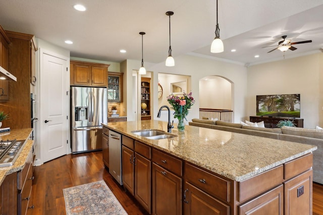 kitchen with arched walkways, a center island with sink, appliances with stainless steel finishes, open floor plan, and a sink