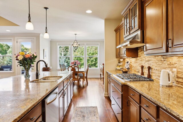 kitchen featuring under cabinet range hood, a sink, appliances with stainless steel finishes, decorative backsplash, and brown cabinetry