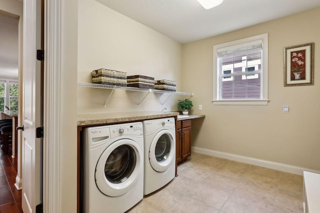 clothes washing area with light tile patterned flooring, washing machine and dryer, cabinet space, and baseboards