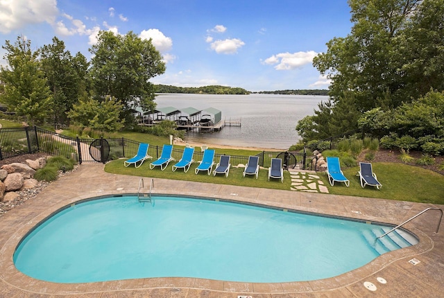 pool with a water view, fence, and a yard