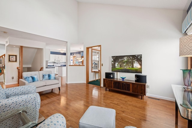 living room with stairway, baseboards, light wood-type flooring, and visible vents