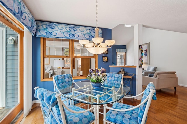 dining room featuring a notable chandelier, lofted ceiling, a textured ceiling, wood finished floors, and baseboards